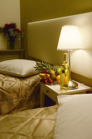 A hotel room with a bedside table featuring a lamp, a fruit bowl, and a bottle. - Phidias Hotel by Oniro (Athens)