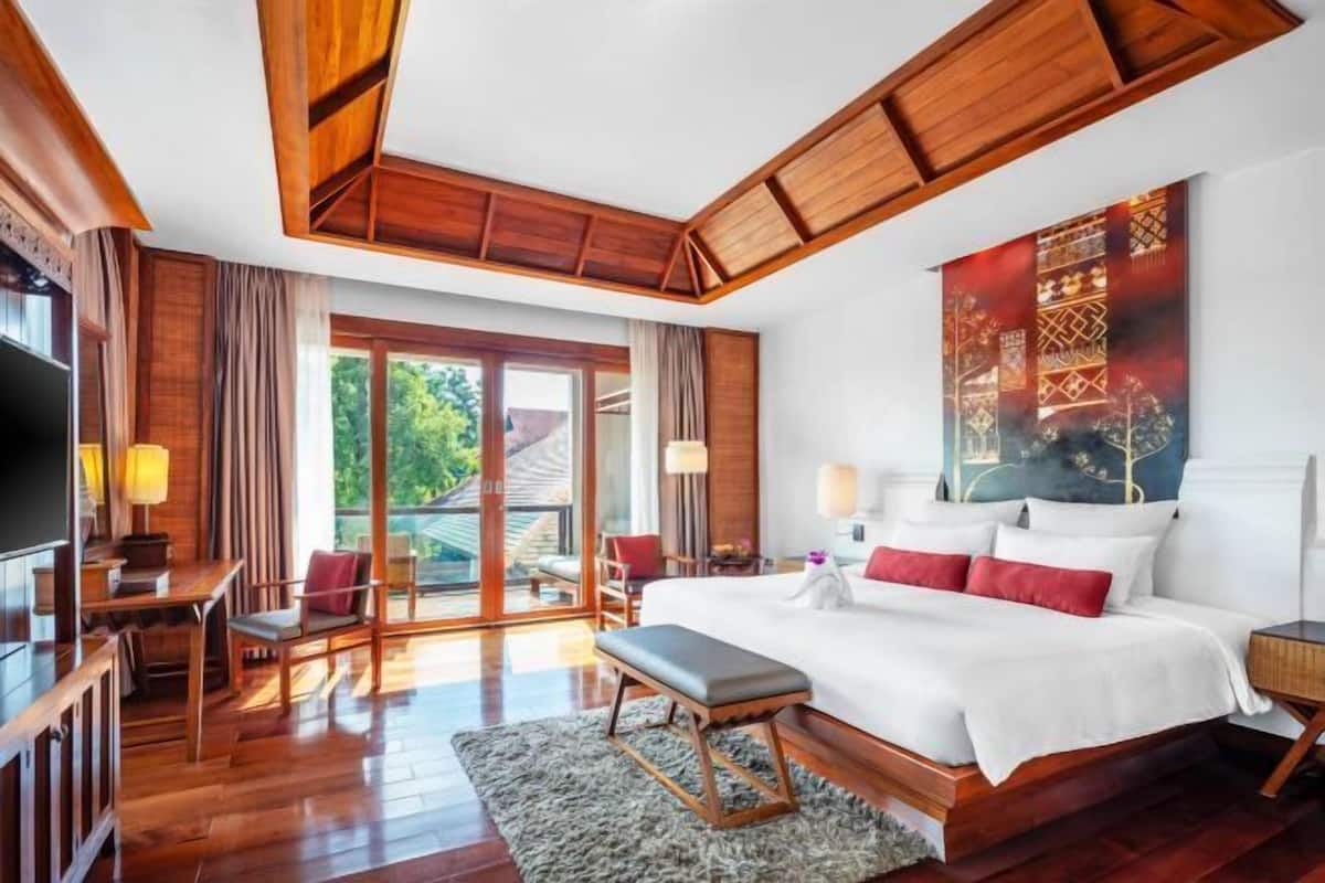 Quarto com cama grande, escrivaninha, cadeira, televisão e vista para o exterior.