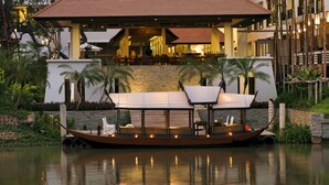Un restaurant situé au bord de l’eau, doté d’une terrasse couverte, d’une piscine et d’un bâtiment moderne en arrière-plan.