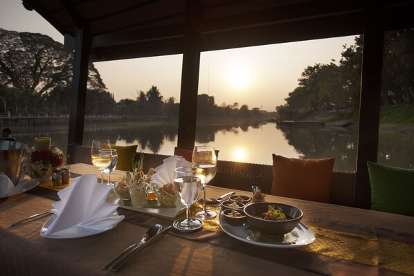 Une table dressée pour un repas, avec vue sur un lac au coucher du soleil.