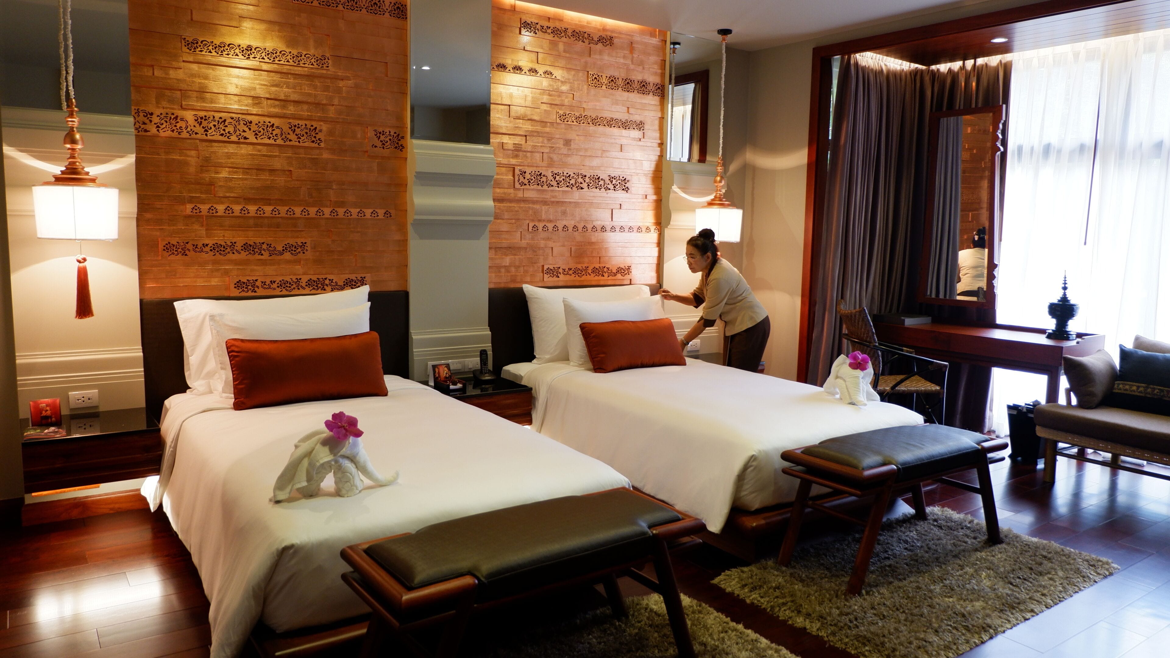 A hotel room with two beds, a desk, a chair, a mirror, and a window with curtains.