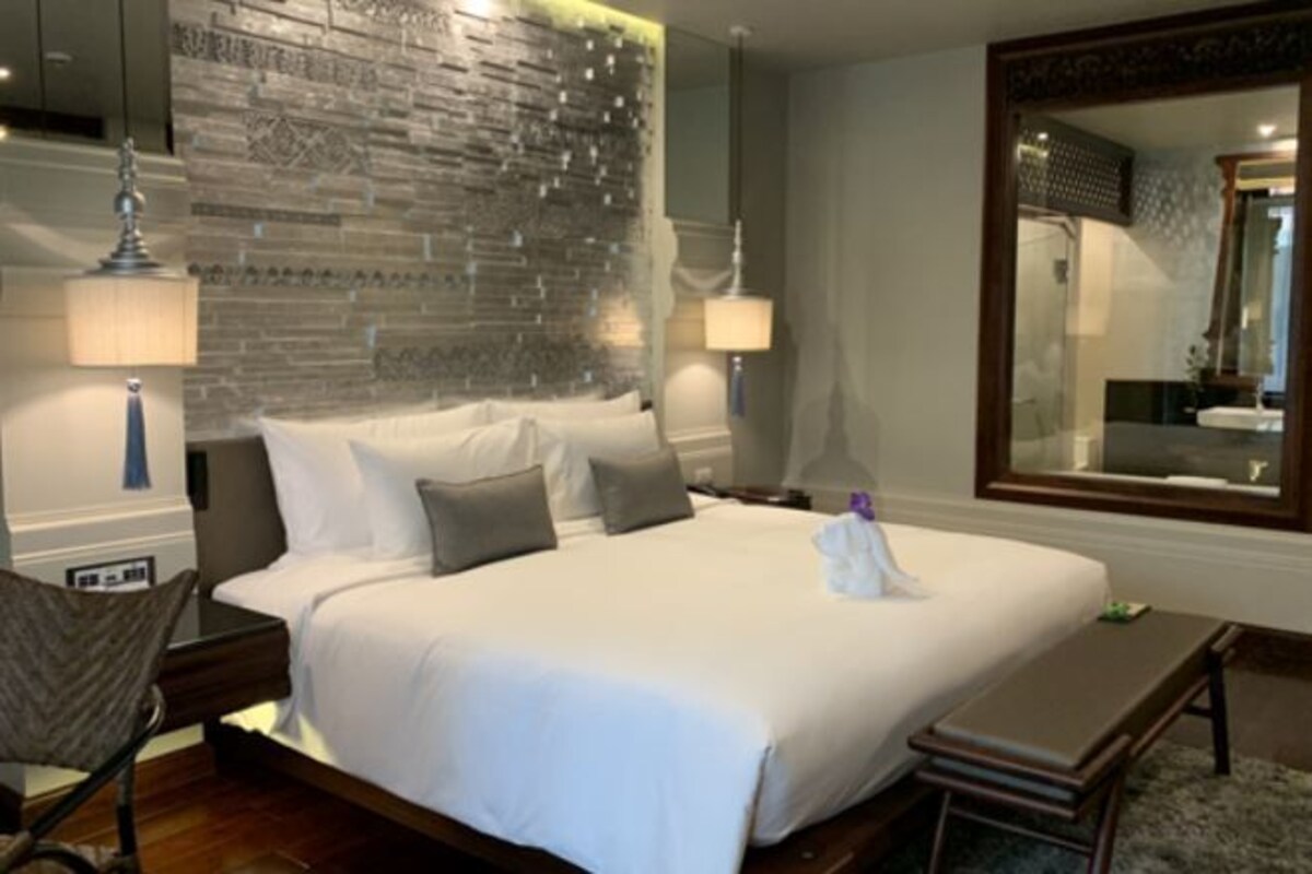 Une chambre d’hôtel avec un grand lit, deux tables de chevet, un banc, un miroir et un mur à motifs.