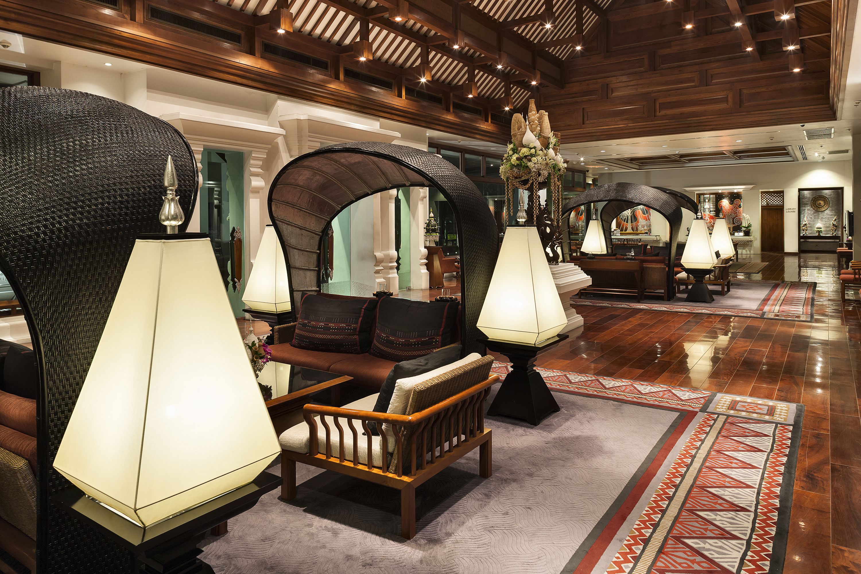A lobby with a seating area, large lamps, and a patterned rug.