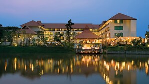 Un grand hôtel à étages, un bateau amarré devant, et un lac paisible qui reflète le bâtiment.