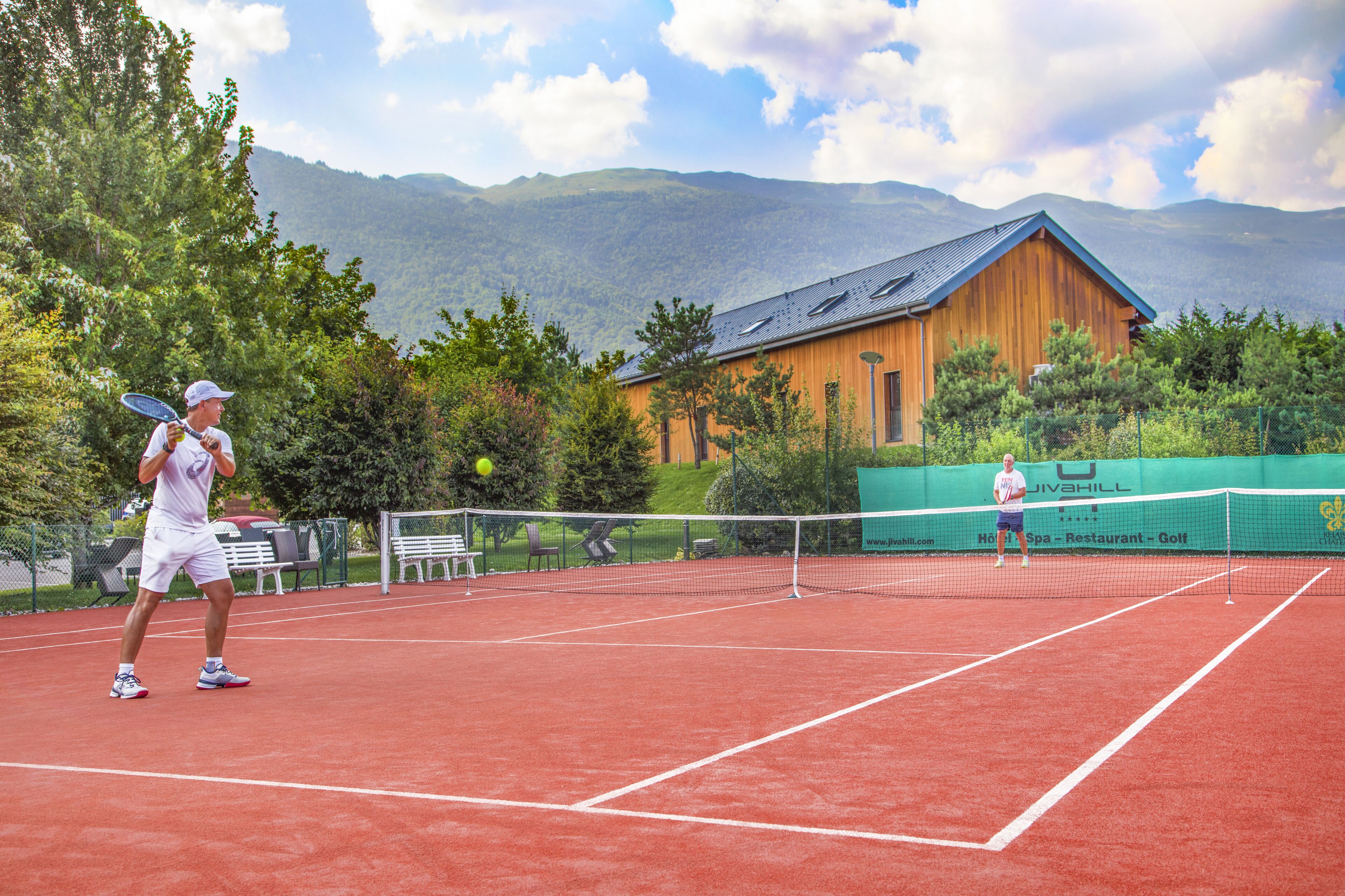 Un court de tennis avec un chalet en bois en arrière-plan et des montagnes au loin.