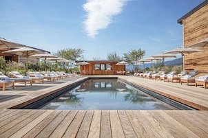 Área de piscina com deck de madeira, cadeiras de descanso e guarda-sóis.