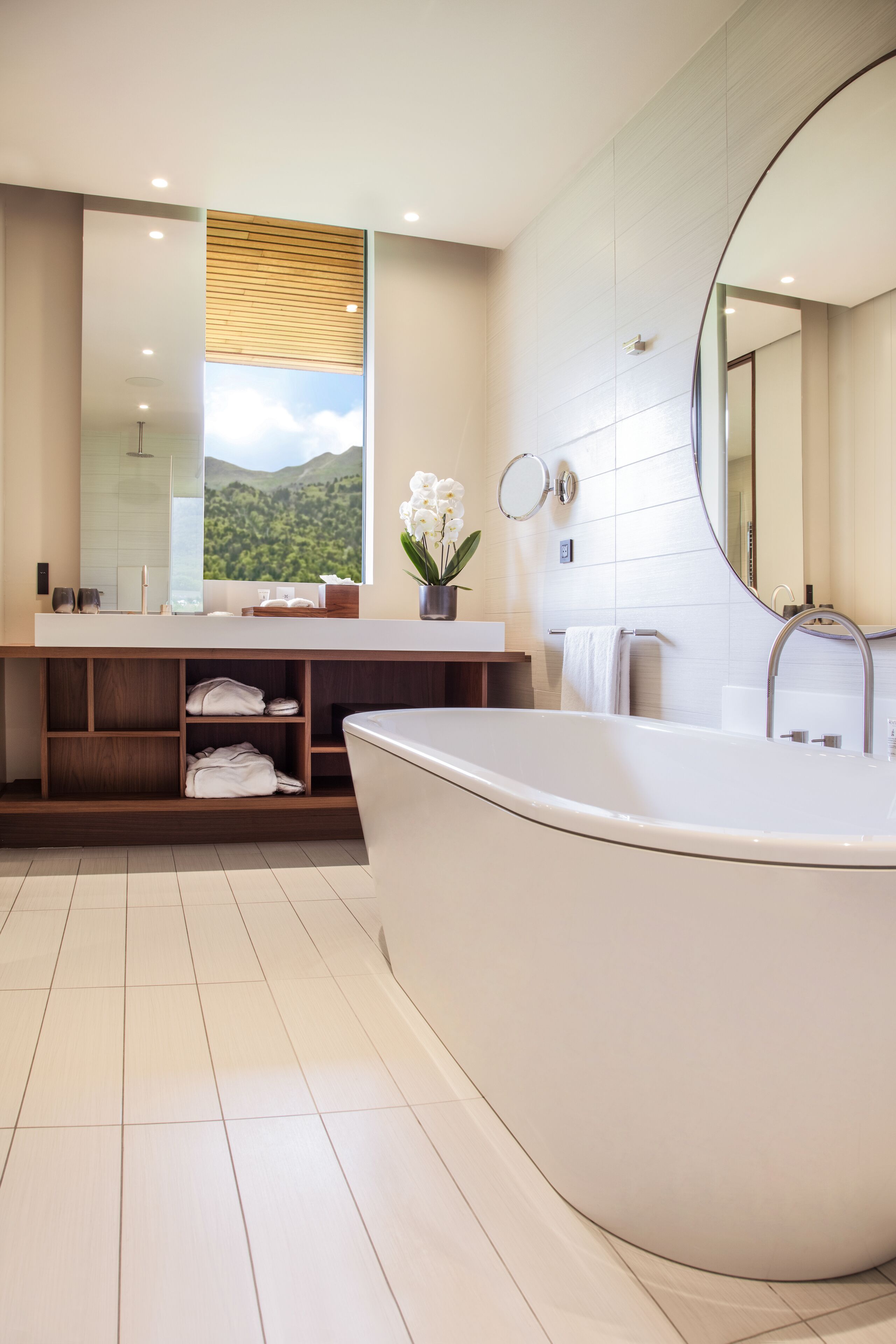A modern bathroom with a large bathtub, a vanity with a mirror, and a window with a view of greenery.