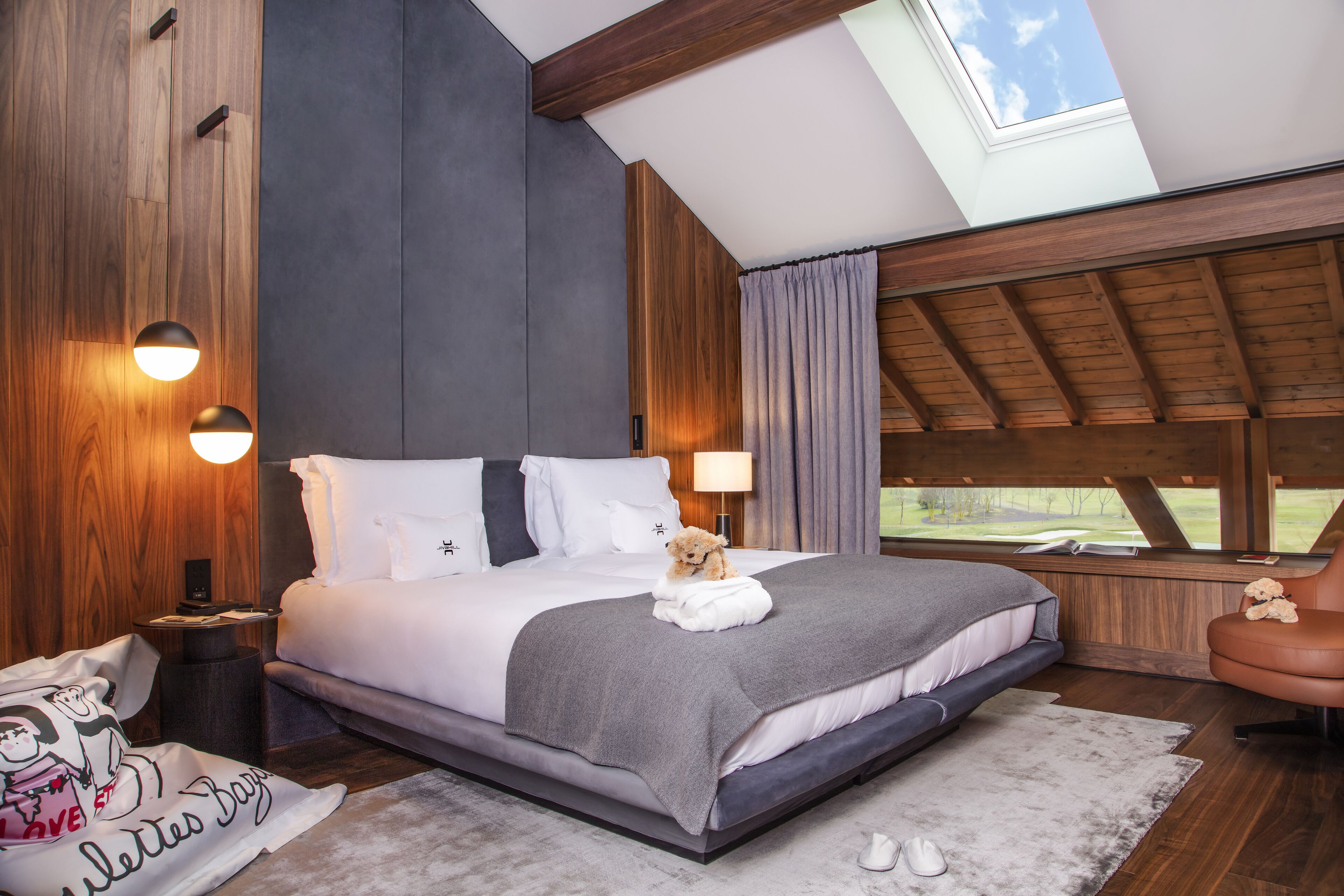 A modern bedroom with a large bed, a skylight, and a view of the outdoors.