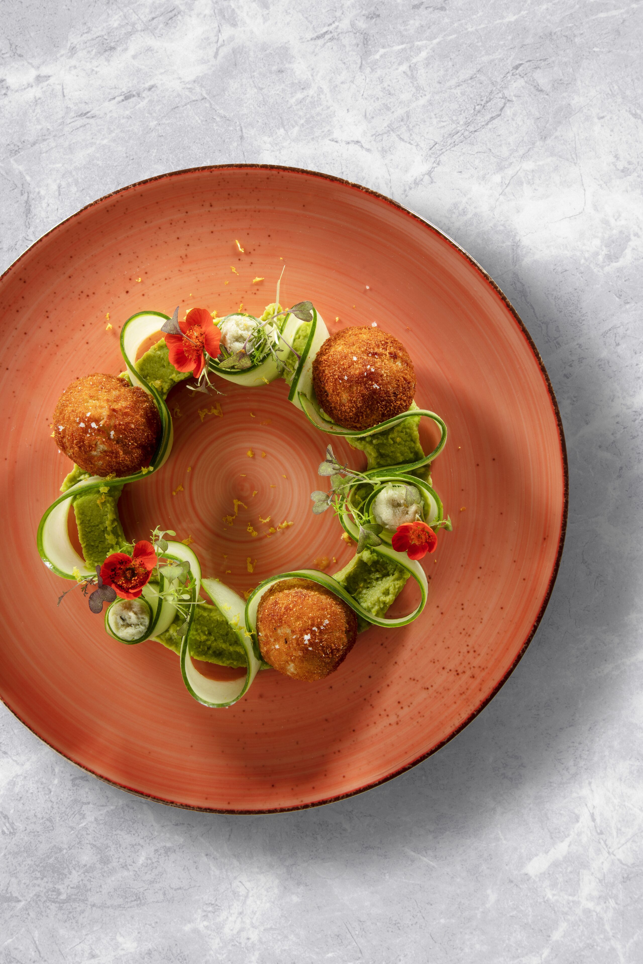 A plate with a circular arrangement of food items, including what appears to be croquettes, cucumber slices, and garnishes.