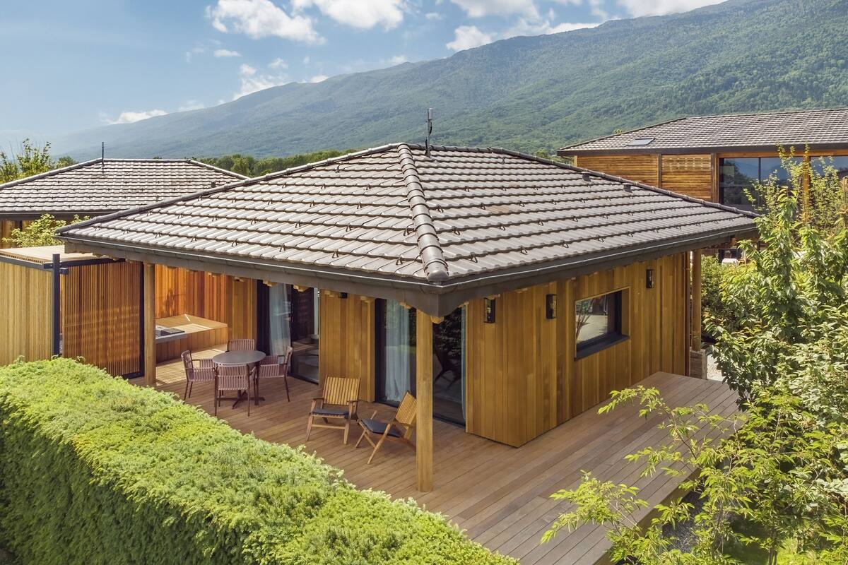 A wooden cabin with a tiled roof, a deck, and a dining area with chairs and a table.
