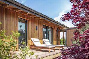 Un edificio moderno de madera con dos sillones en una terraza al aire libre.