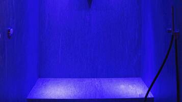 Een kamer met blauw licht, een driehoekig embleem aan de muur, een bank en een douchekop.