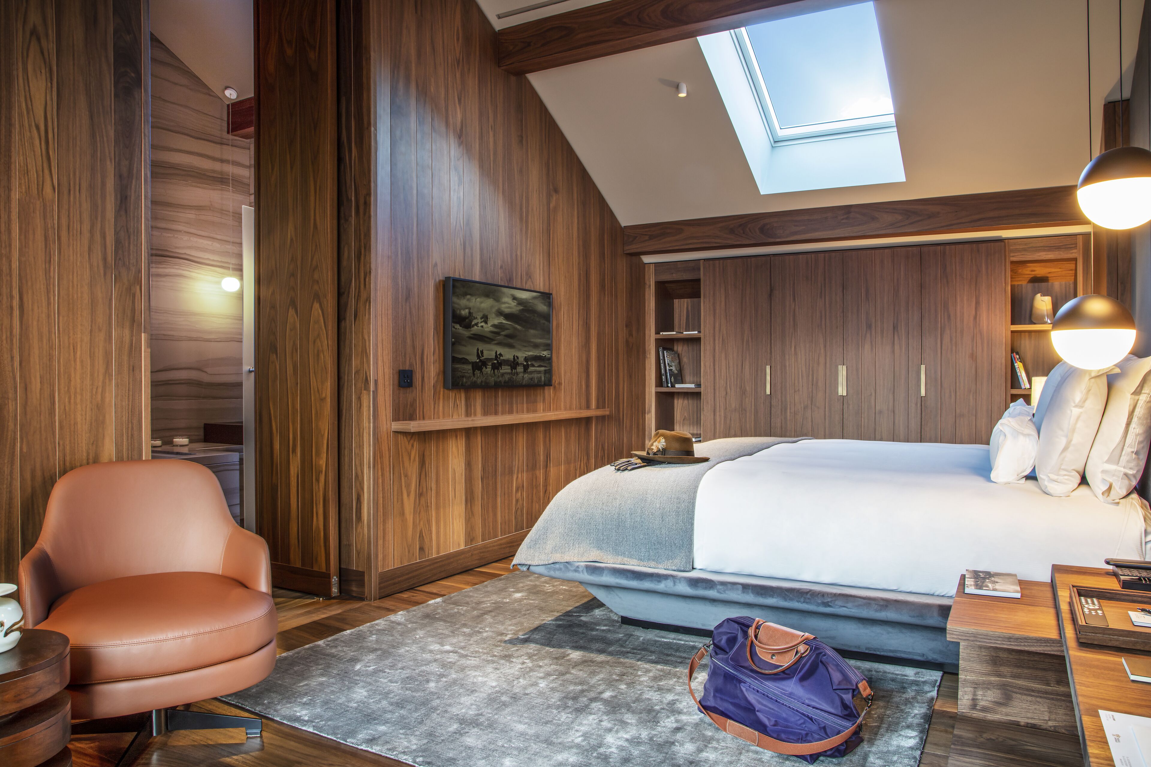 A modern hotel room with a skylight, wooden paneling, a large bed, a seating area, and a wardrobe.