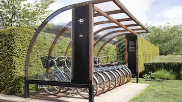 A bike rental station with a transparent roof and wooden structure, surrounded by greenery.