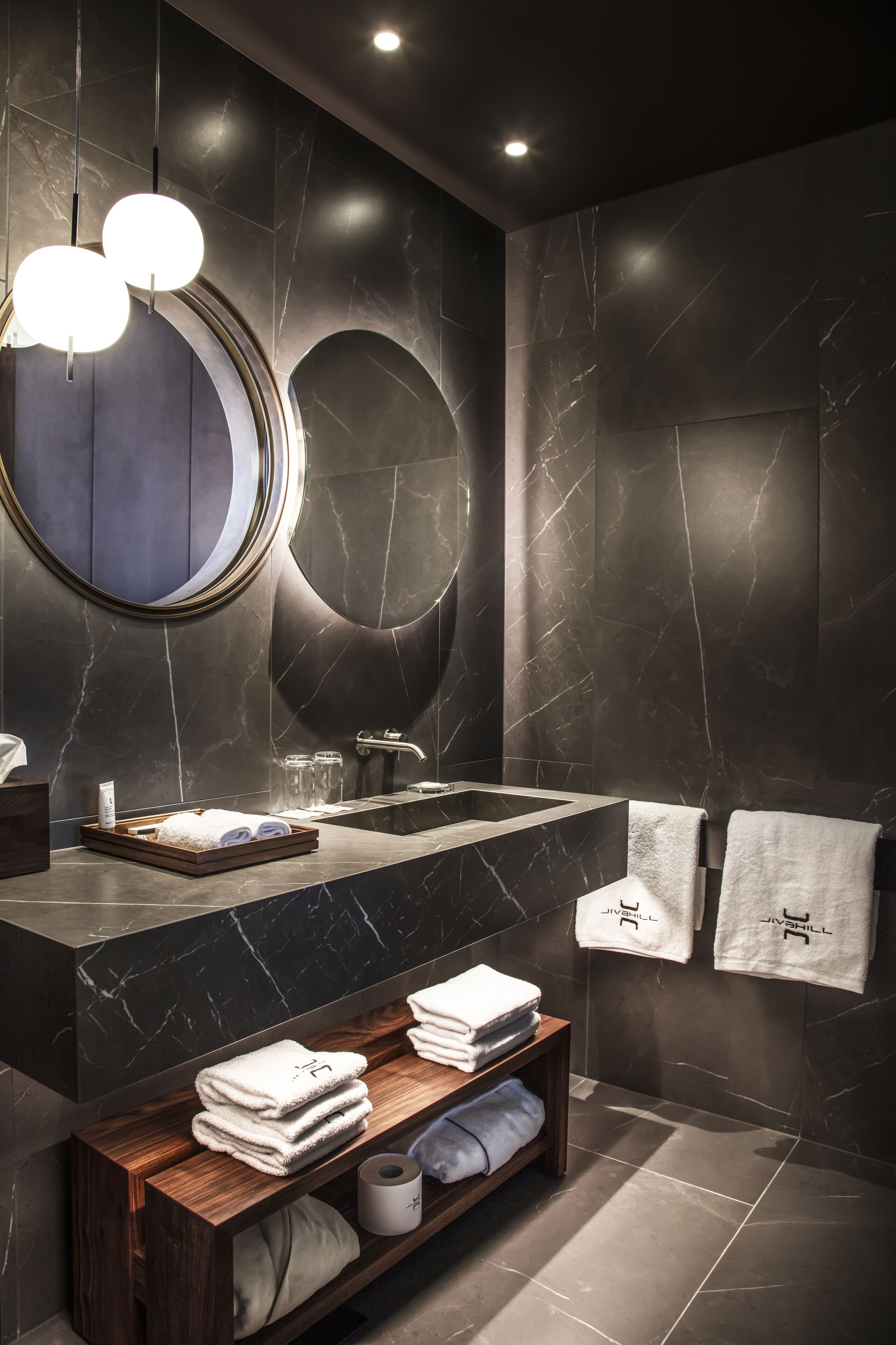 Un baño moderno con tocador de mármol, dos espejos redondos y toallas ordenadas.