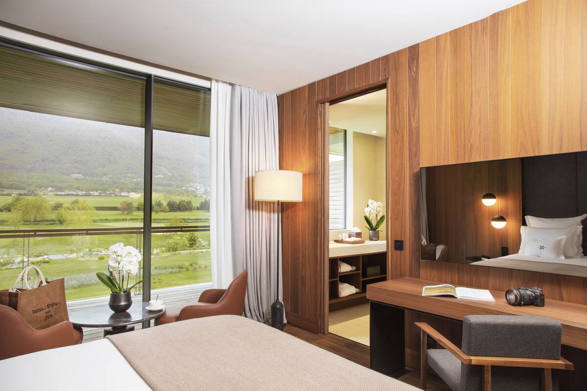A hotel room with a large window, a bed, a desk, and a chair.