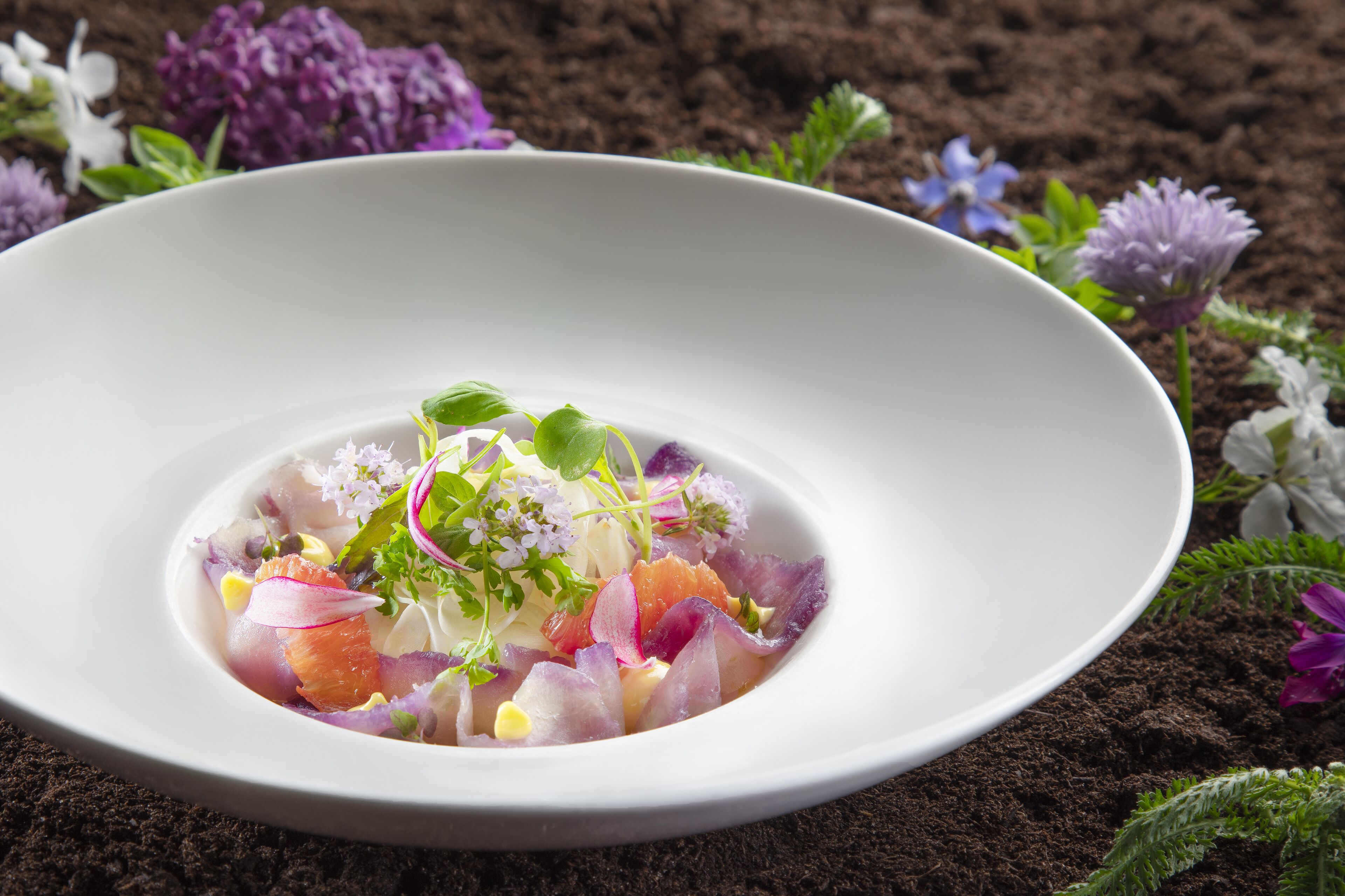 A white bowl of colorful salad with various vegetables and herbs.