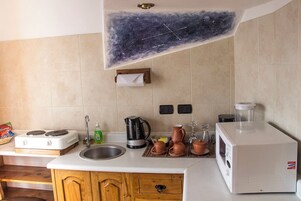 Een keuken met een fornuis, spoelbak en een magnetron. Op het aanrecht staan pannen, een waterkoker en een blender.
