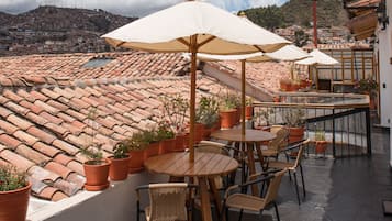 Una terraza al aire libre con mesas y sillas de madera, plantas en macetas y sombrillas.