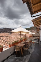 Una terraza al aire libre con mesas y sillas de madera, plantas en macetas y sombrillas.