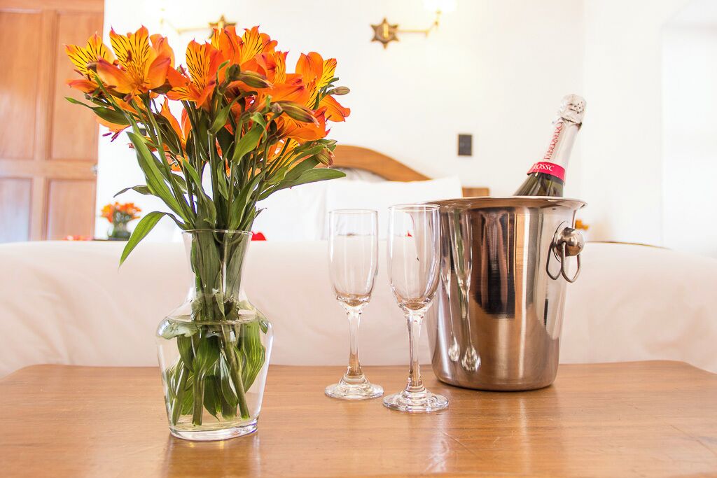 A table with a vase of orange flowers, two empty glasses, and a champagne bucket with a bottle.