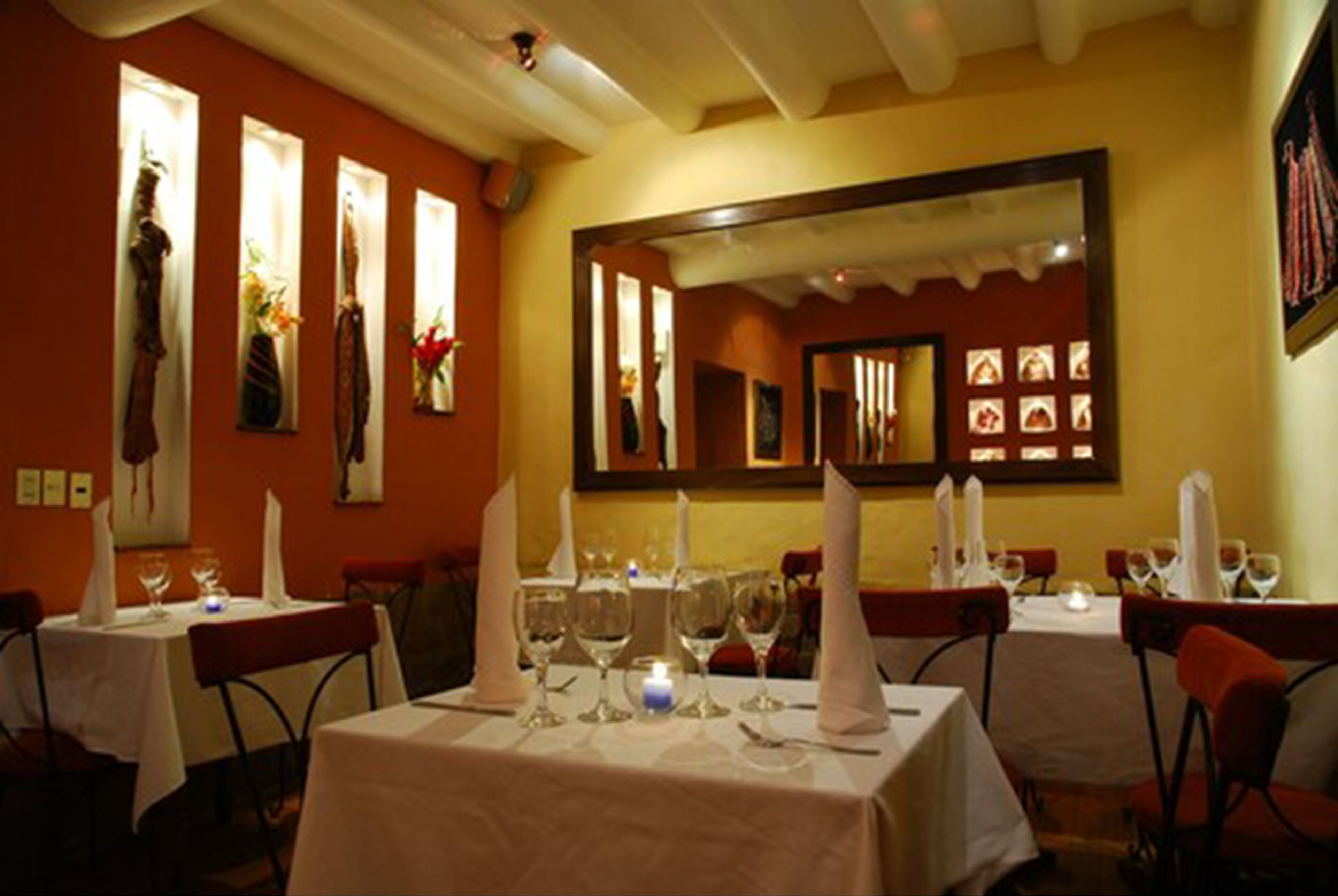 Un restaurante con mesas dispuestas para comer, que incluye un espejo en la pared y obras de arte enmarcadas.