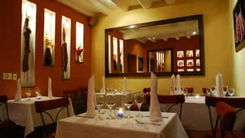 Un restaurante con mesas dispuestas para comer, que incluye un espejo en la pared y obras de arte enmarcadas.