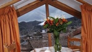 A wooden table with a vase of flowers, two chairs, and a view of a cityscape through a window. - Casa San Blas Boutique Hotel (Cusco)