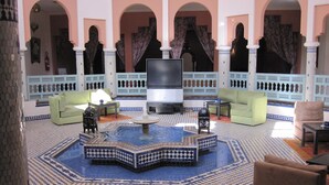 Un hall d’entrée spacieux avec une fontaine centrale, plusieurs espaces aménagés pour s’asseoir et un grand téléviseur à écran plat.
