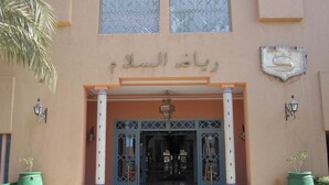 Une entrée d’immeuble avec une enseigne en arabe, deux grandes fenêtres et deux jardinières vertes.