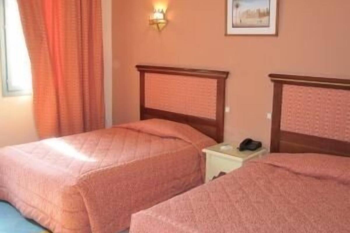 A room with two beds, a nightstand, a wall-mounted light, and a framed picture.