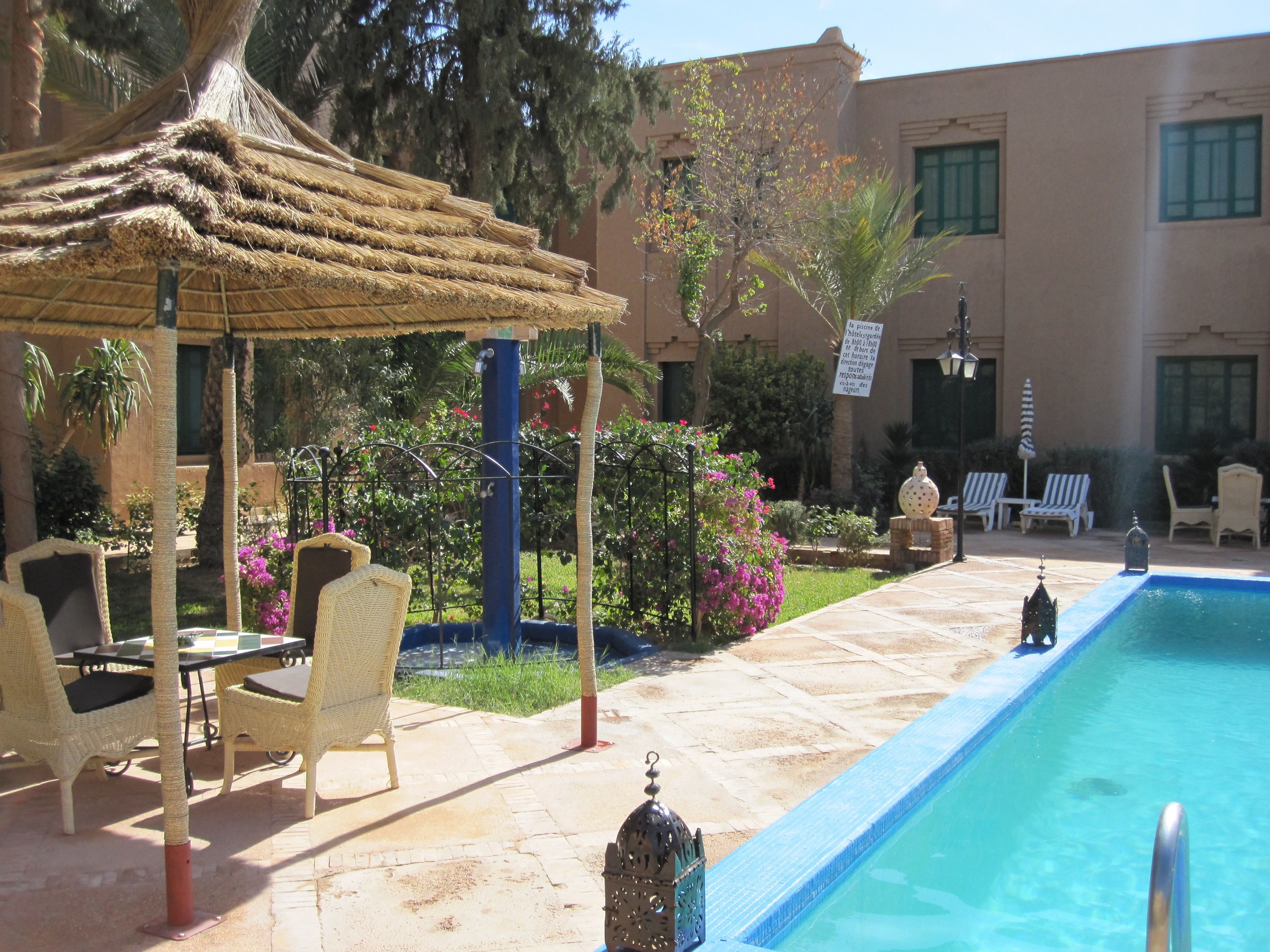 Un espace aménagé au bord de la piscine, avec un gazebo à toit de chaume, des fauteuils en osier et une piscine.