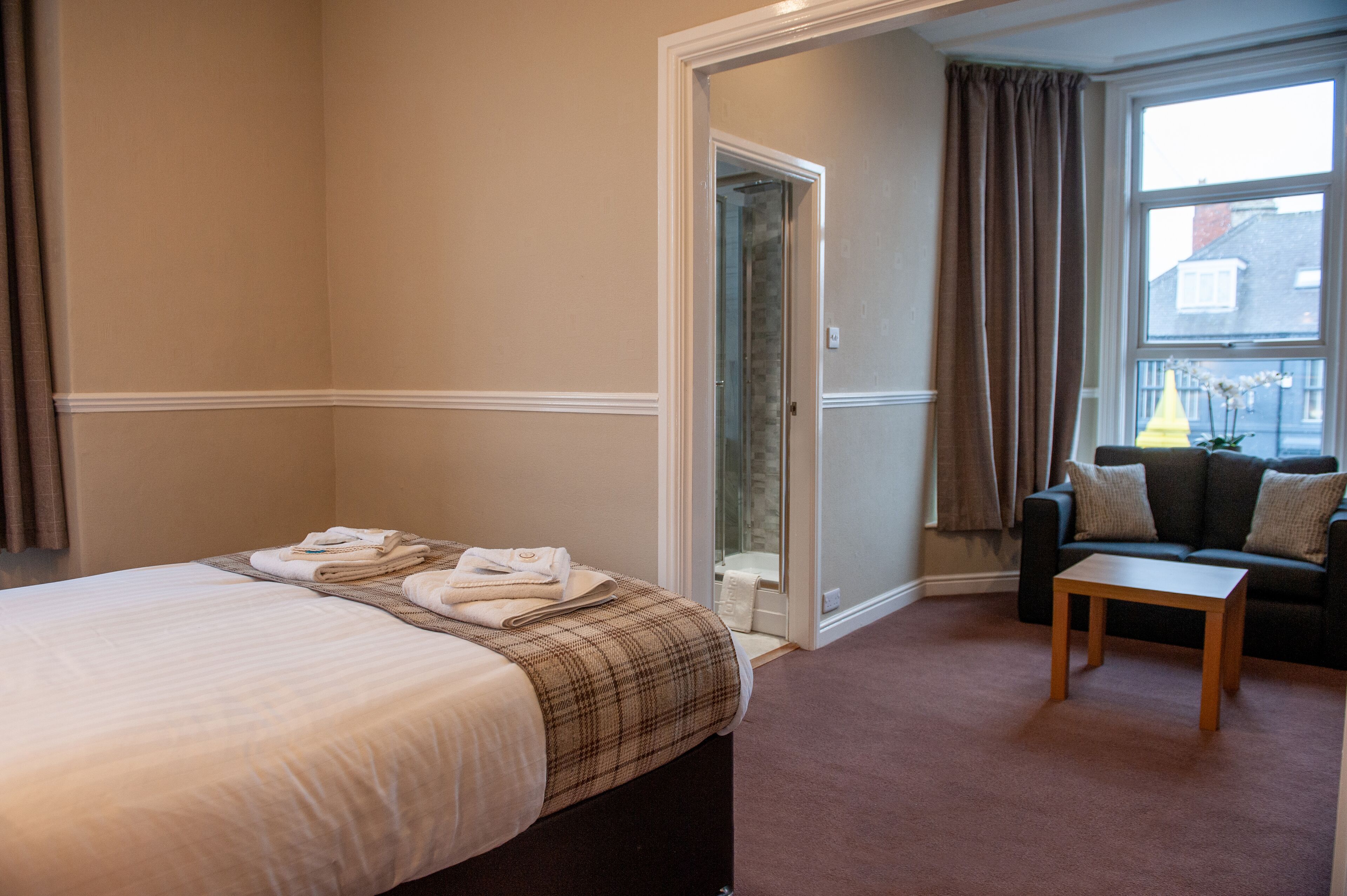 A hotel room with a bed, a small table, a sofa, and a window with curtains.