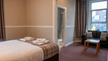 A hotel room with a bed, a small table, a sofa, and a window with curtains.