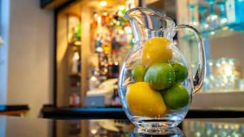 A clear glass pitcher filled with lemons and limes on a reflective surface.