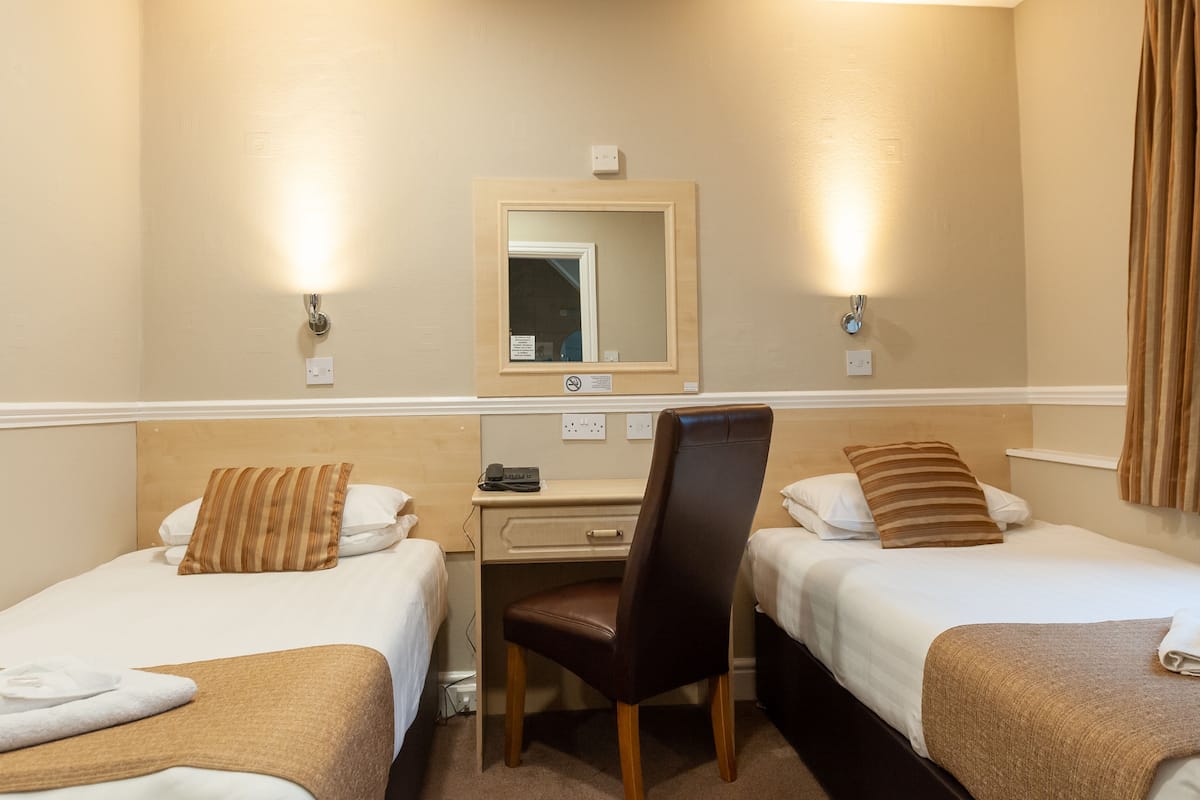 A hotel room with two beds, a desk, a chair, and a mirror.
