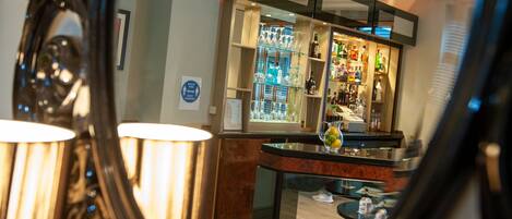 A bar area with shelves of bottles and glasses, a counter, and a decorative lamp.