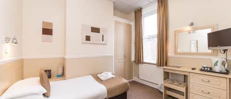 Habitación de hotel con cama, escritorio, silla, televisor y ventana con cortinas.