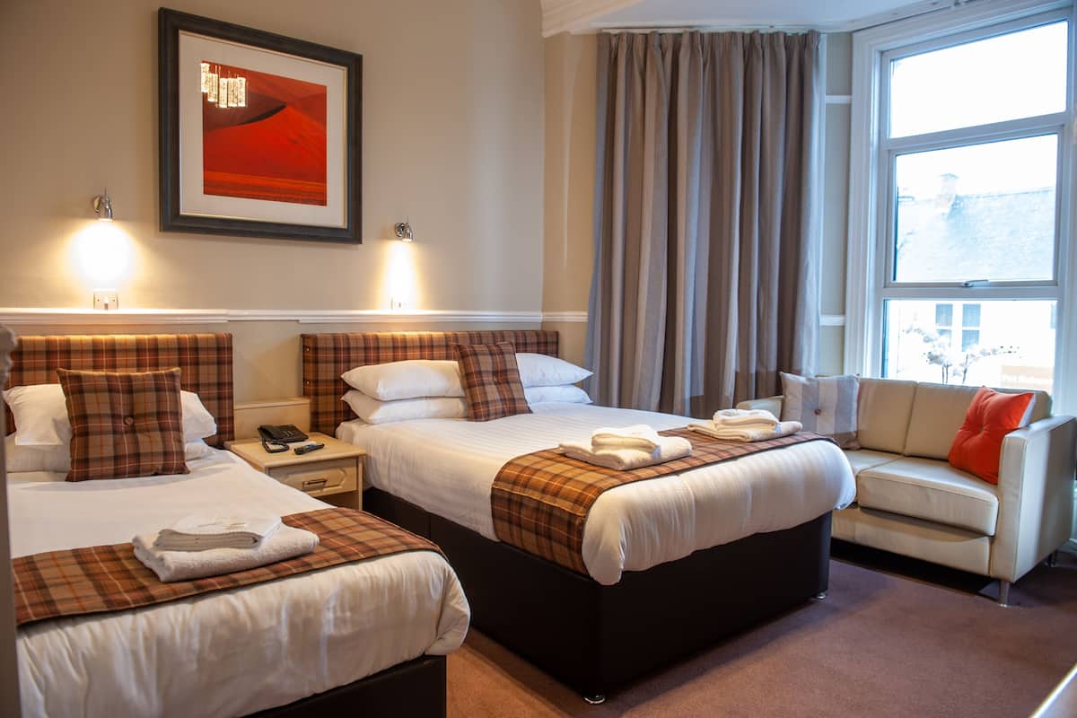 A hotel room with two beds, a sofa, and a large window.