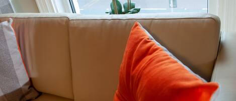 A beige sofa with a red cushion and a white cushion.
