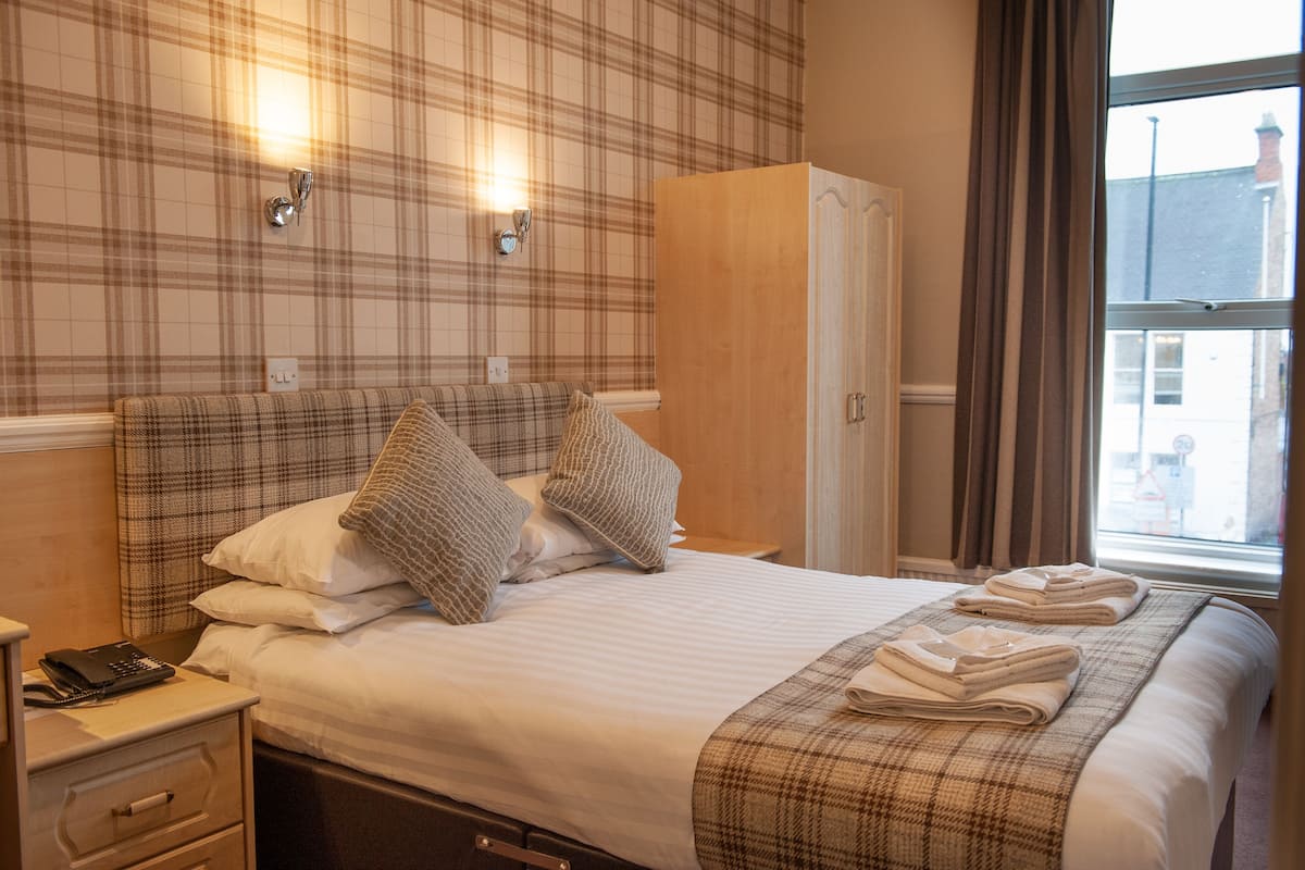 A hotel room with a plaid-patterned headboard, a bedside table with a phone, and a window with curtains.