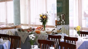 Un comedor con mesas dispuestas para el desayuno, que incluye diversos alimentos y un jarrón con flores.