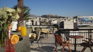 Una terraza con asientos al aire libre, vista de un paisaje urbano y un cartel anunciando un evento.