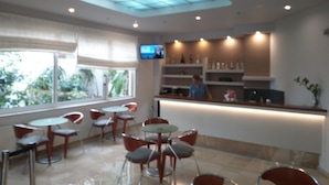Un restaurante moderno con techo de vidrio, una televisión montada en la pared y una barra con una persona detrás.