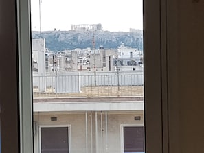 A view of a cityscape with a prominent ancient Greek temple in the background, modern buildings, and a fenced area in the foreground.