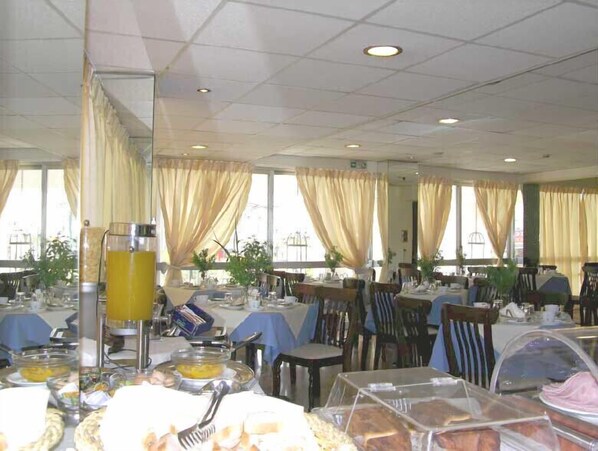 A large dining area with multiple tables and chairs, a buffet setup with various food items, and large windows with curtains.