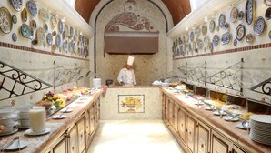 Una cocina con un chef, un mostrador de buffet con diversos platos, y platos decorativos en las paredes.