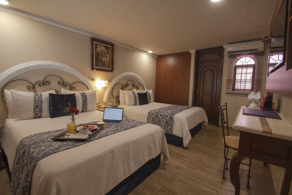 Habitación de hotel con dos camas, un escritorio, una silla y una ventana con persianas.