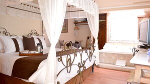 Una cama bien tendida con dosel, una mesita de noche con lámpara y una ventana con persianas.