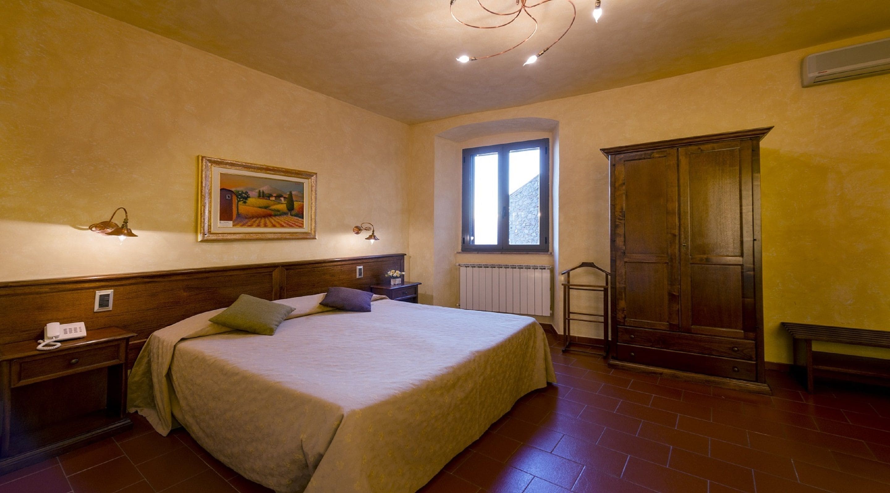 A bedroom with a bed, bedside tables, a wardrobe, a window, and a painting on the wall.